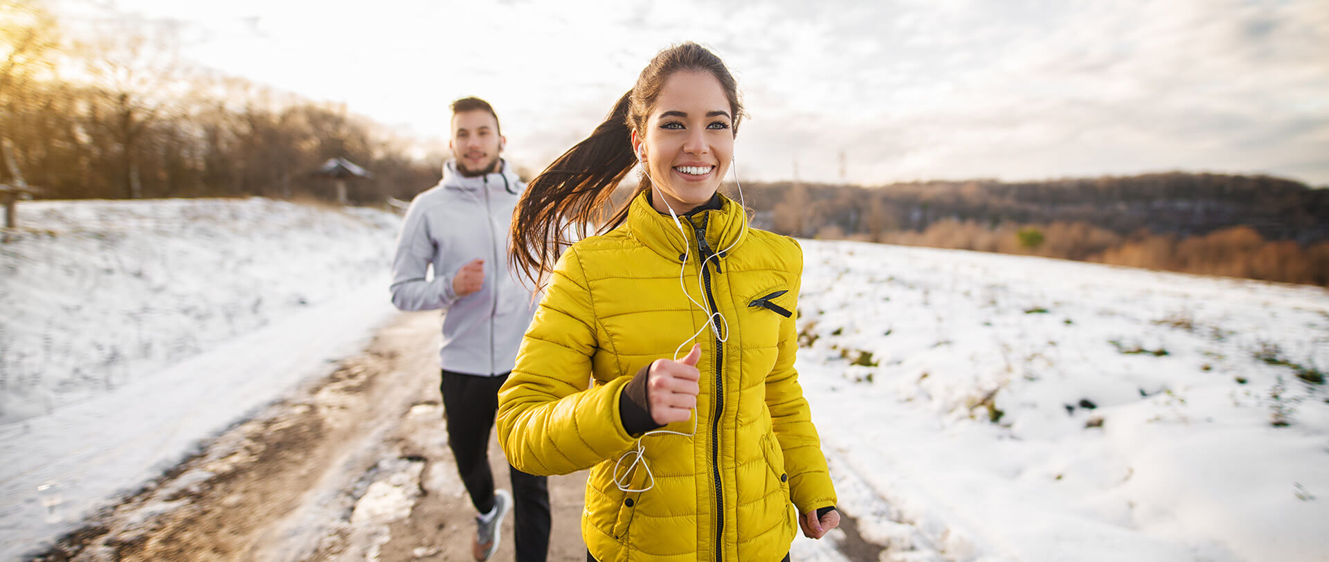 Smiling couple running along a snowy, wintry road.