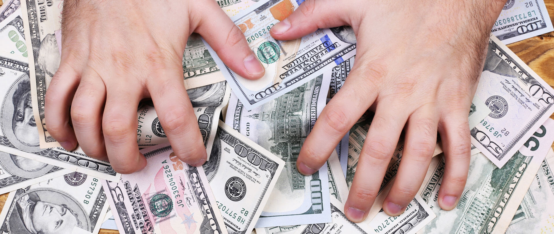 Two hands claw at a pile of U.S. dollar bills