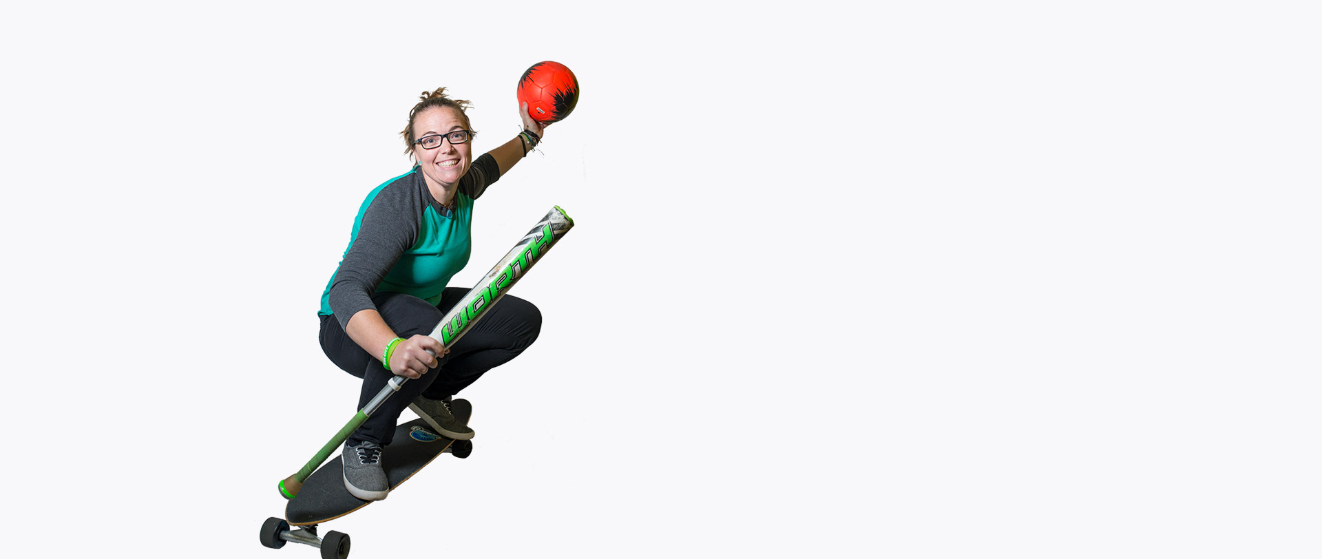 Our Health Coach Manager, Katy O’Farrell, riding a skateboard while holding a baseball bat in one hand and a red soccer ball in the other.