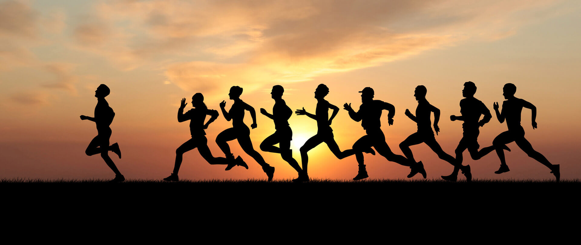 Marathon runners, silhouetted against a sunset, dash toward the finish line.