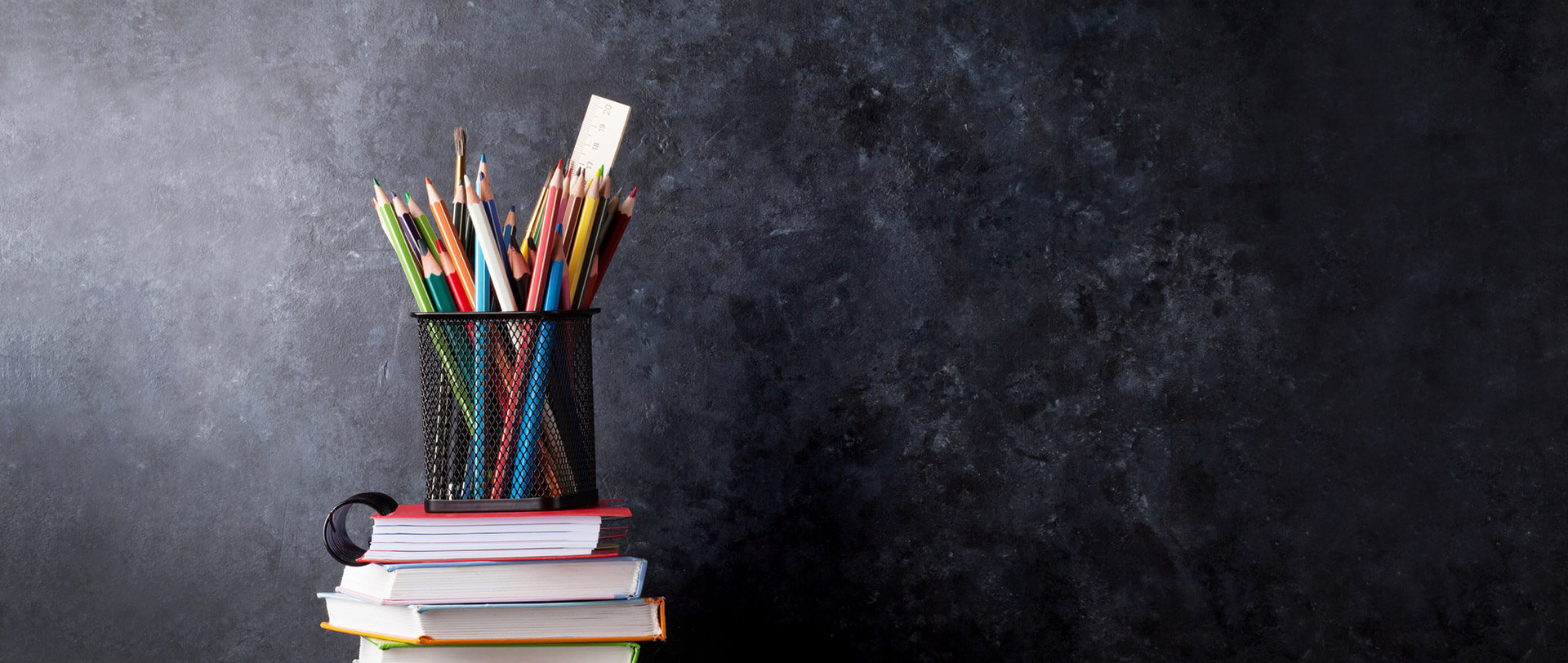 A black chalkboard, with colorful school supplies in the foreground.